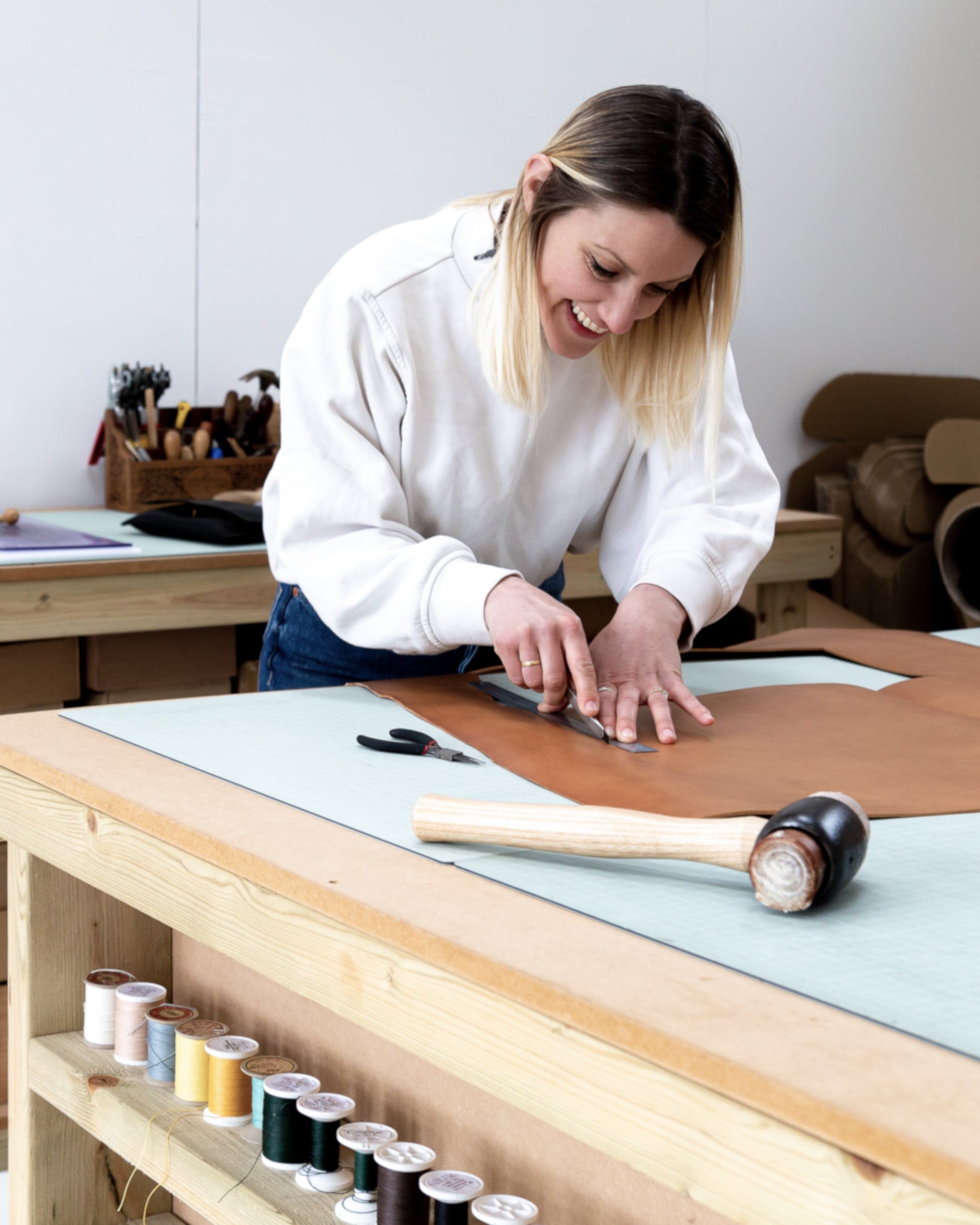 Becky from British Leather Supplies working at a table with leather and tools in a workshop setting