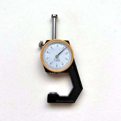 A dial micrometer caliper with a black body, silver metal jaws, and a white face with a yellow-orange bezel, photographed on a plain white background.