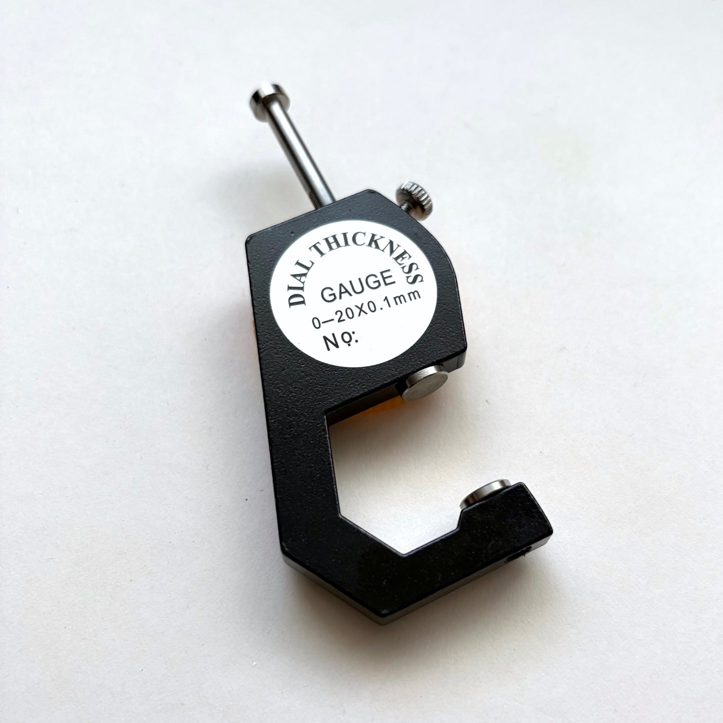 A black dial thickness gauge with a silver metal probe and a white circular label that reads 'DIAL THICKNESS GAUGE 5/8 0-20X0.1mm N°9'.