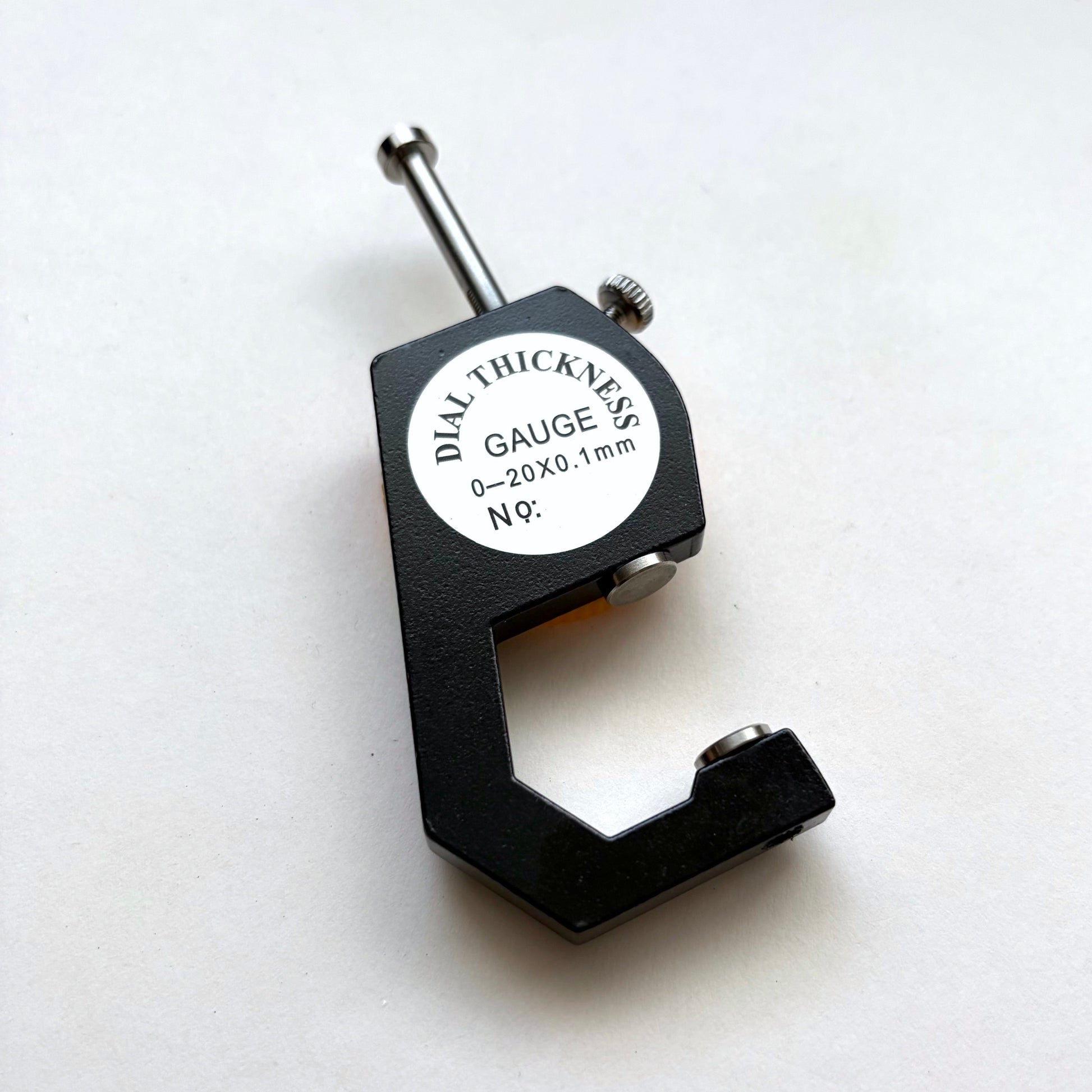 A black dial thickness gauge with a silver metal probe and a white circular label that reads 'DIAL THICKNESS GAUGE 5/8 0-20X0.1mm N°9'.