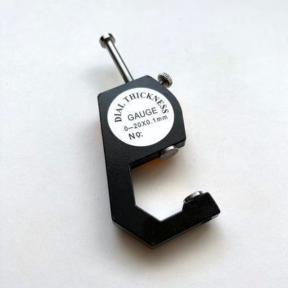 A black dial thickness gauge with a silver metal probe and a white circular label that reads 'DIAL THICKNESS GAUGE 5/8 0-20X0.1mm N°9'.