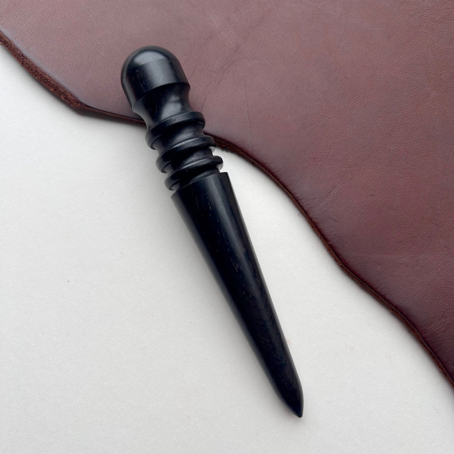 Black ebony leather burnishing tool on a brown leather surface