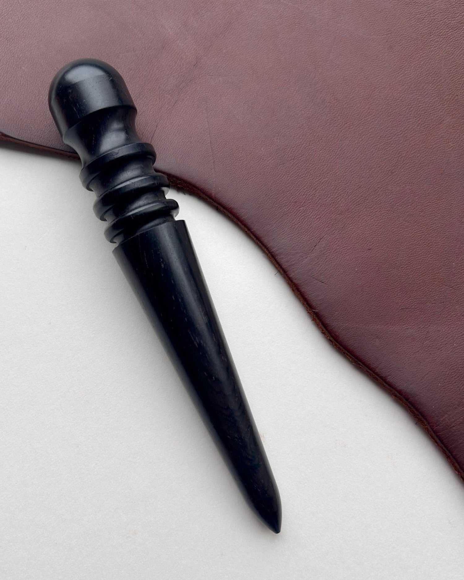 Black ebony leather burnishing tool on a brown leather surface