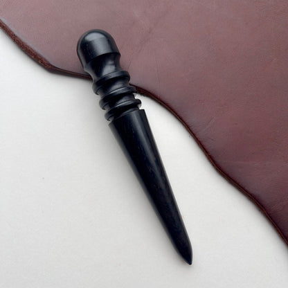 Black ebony leather burnishing tool on a brown leather surface