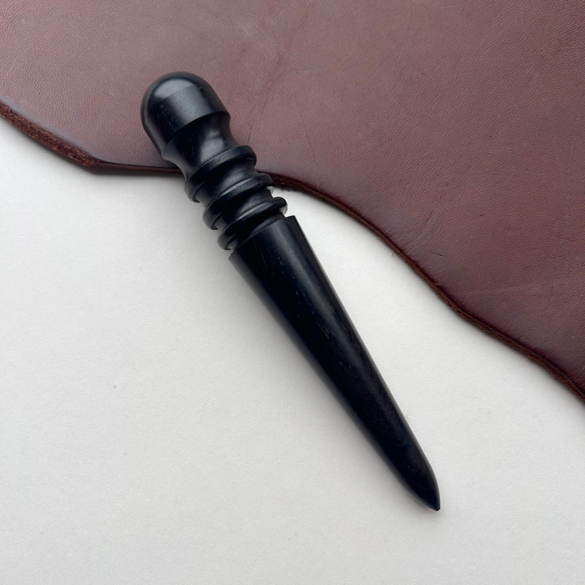 Black wooden leather burnishing tool on a brown leather surface