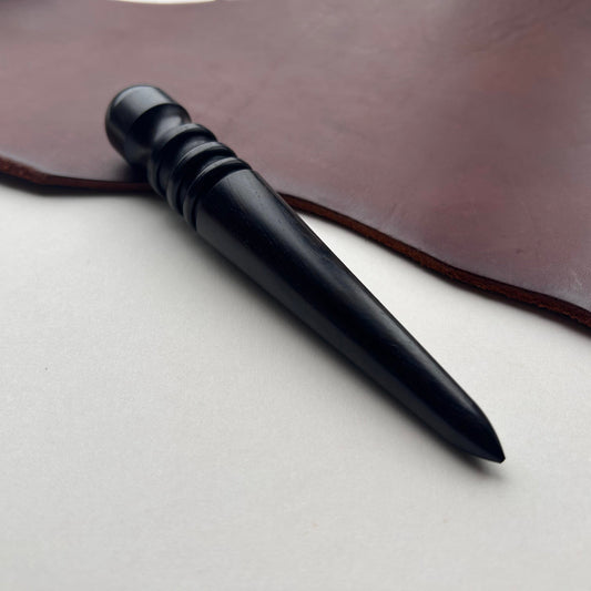 Black wooden leather burnishing tool on a brown leather surface