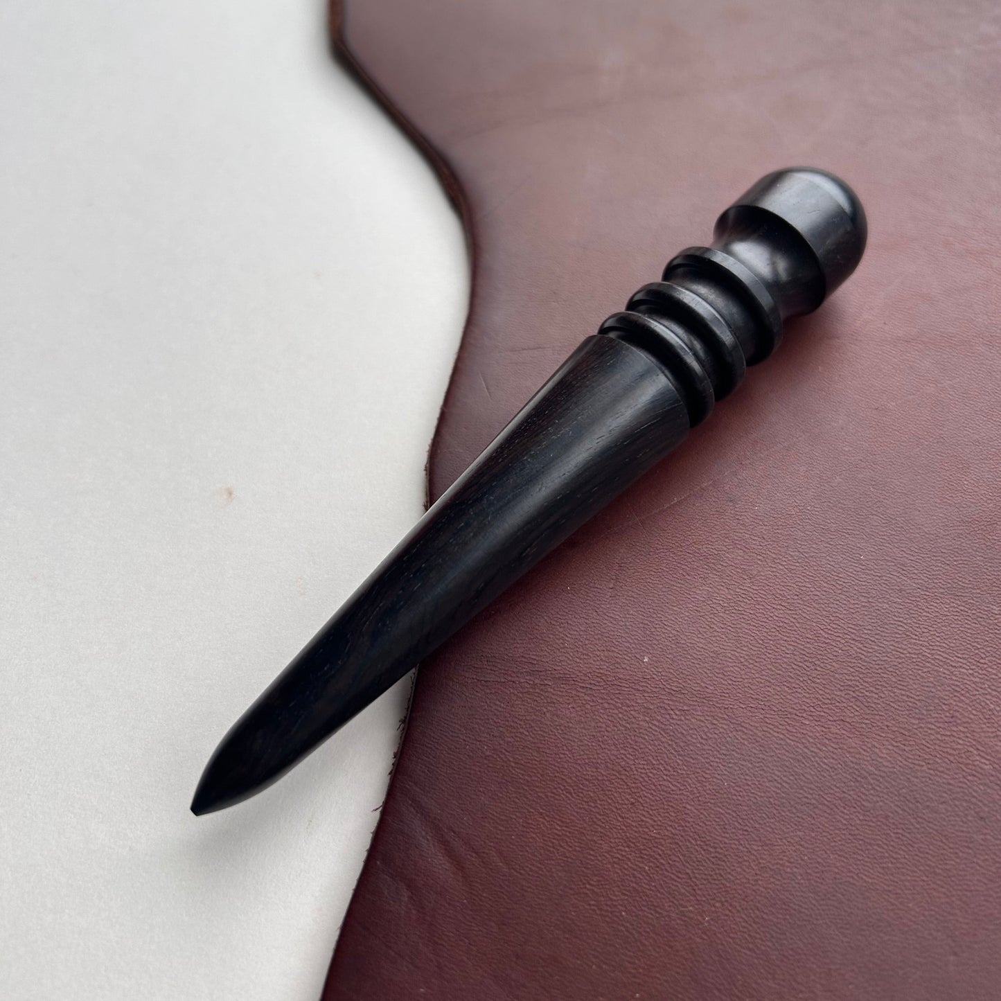 Black wooden leather burnishing tool on a brown and white background