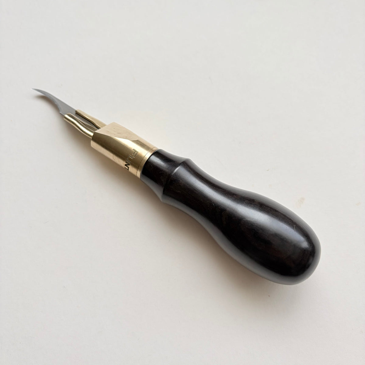 A leather clicker knife with a polished dark wood handle and a brass collar, featuring a curved metal blade, photographed on a plain off-white background.