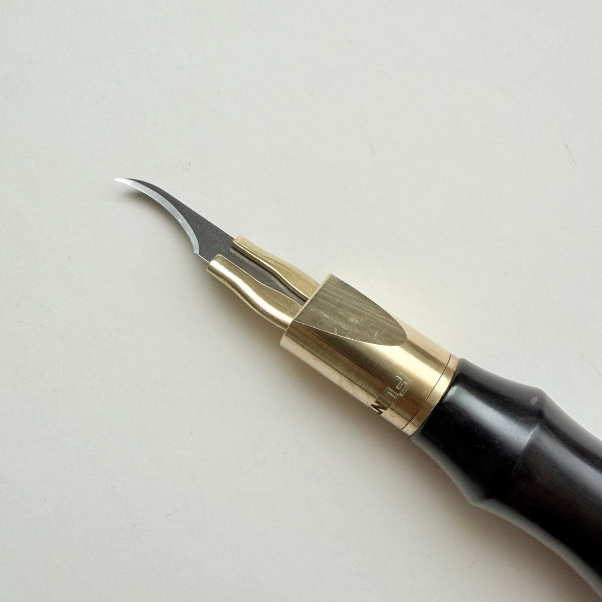 A leather clicker knife tool with a black wooden handle, brass collar, and sharp silver metal blade, photographed on a plain light background.