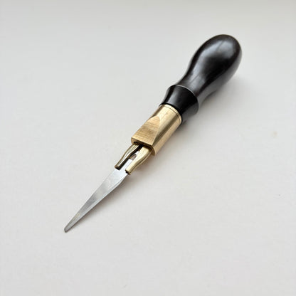 A leather clicker knife tool with a black wooden handle, brass collar, and sharp silver metal blade, photographed on a plain light background.