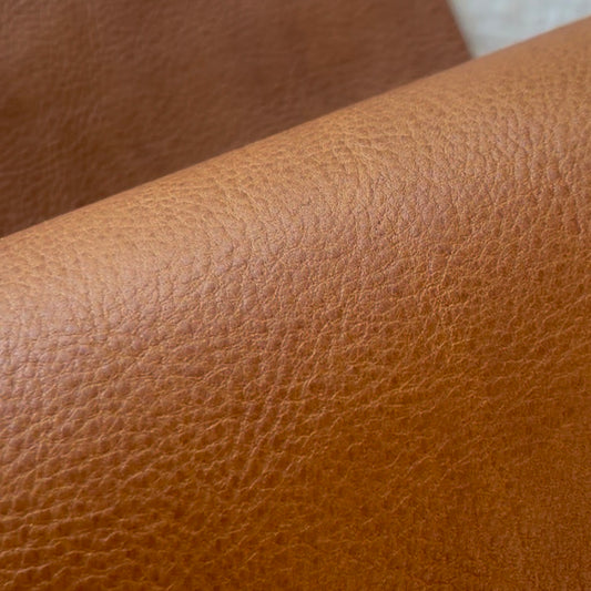 A close-up of a rolled piece of textured brown badalassi carlo minerva box leather showing its pebbled grain surface.