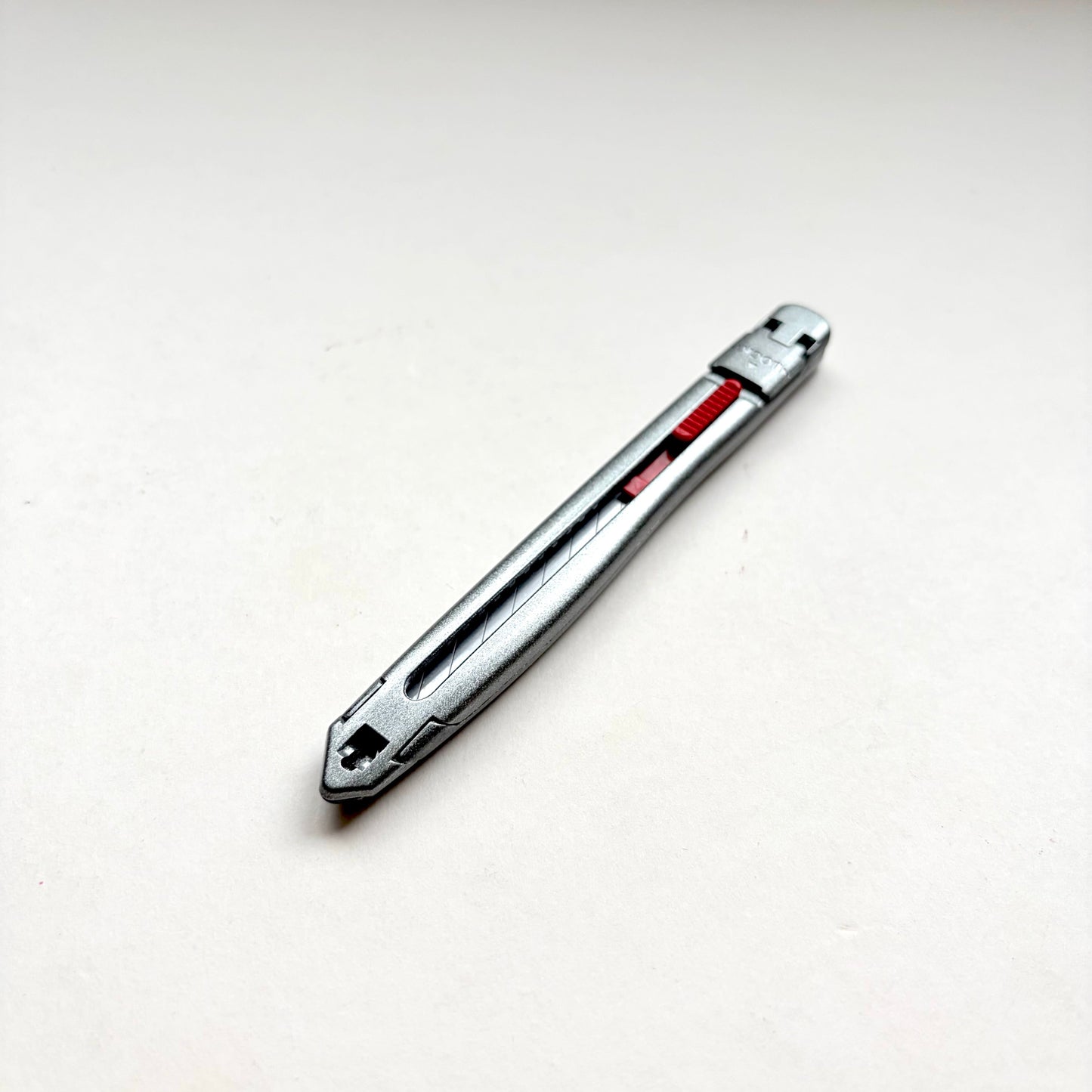 A silver Glanz utility knife with a red sliding scale indicator, shown diagonally on a plain off-white background.