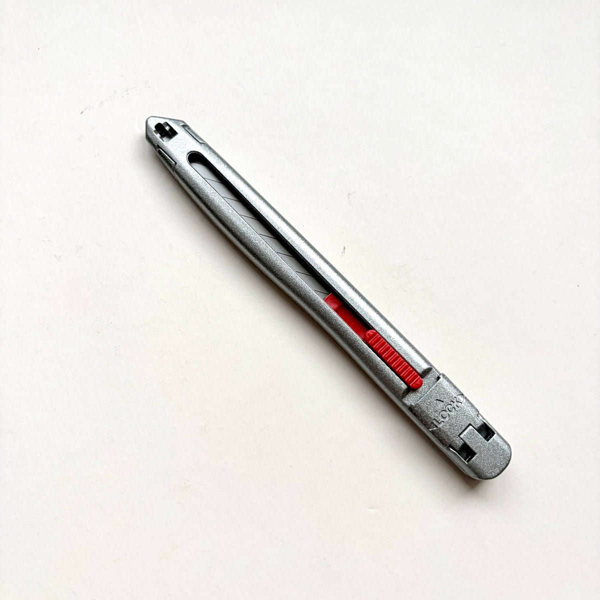 A silver Glanz utility knife with a red sliding scale indicator, shown diagonally on a plain off-white background.