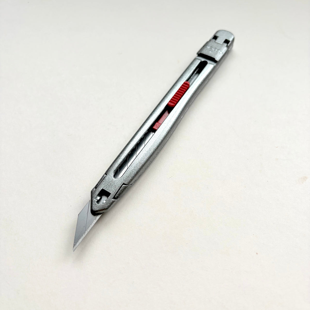 A silver Glanz utility knife with a red sliding scale indicator, shown diagonally on a plain off-white background.