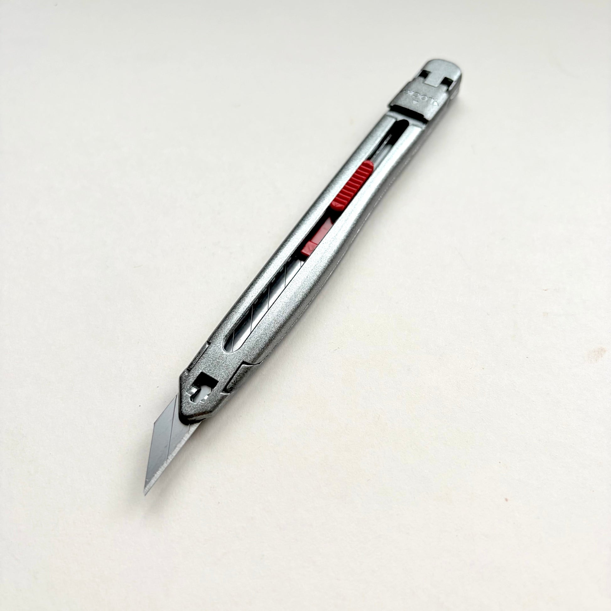 A silver Glanz utility knife with a red sliding scale indicator, shown diagonally on a plain off-white background.