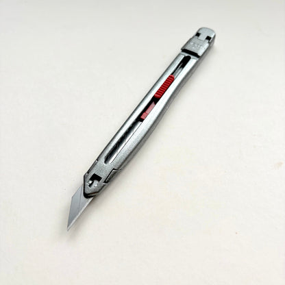 A silver Glanz utility knife with a red sliding scale indicator, shown diagonally on a plain off-white background.