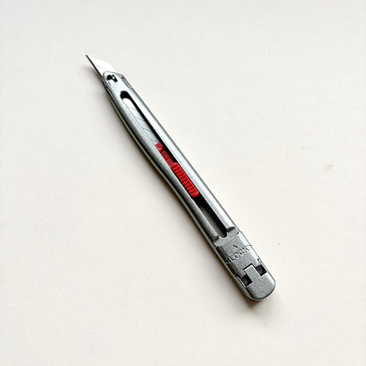 A silver Glanz utility knife with a red sliding scale indicator, shown diagonally on a plain off-white background.