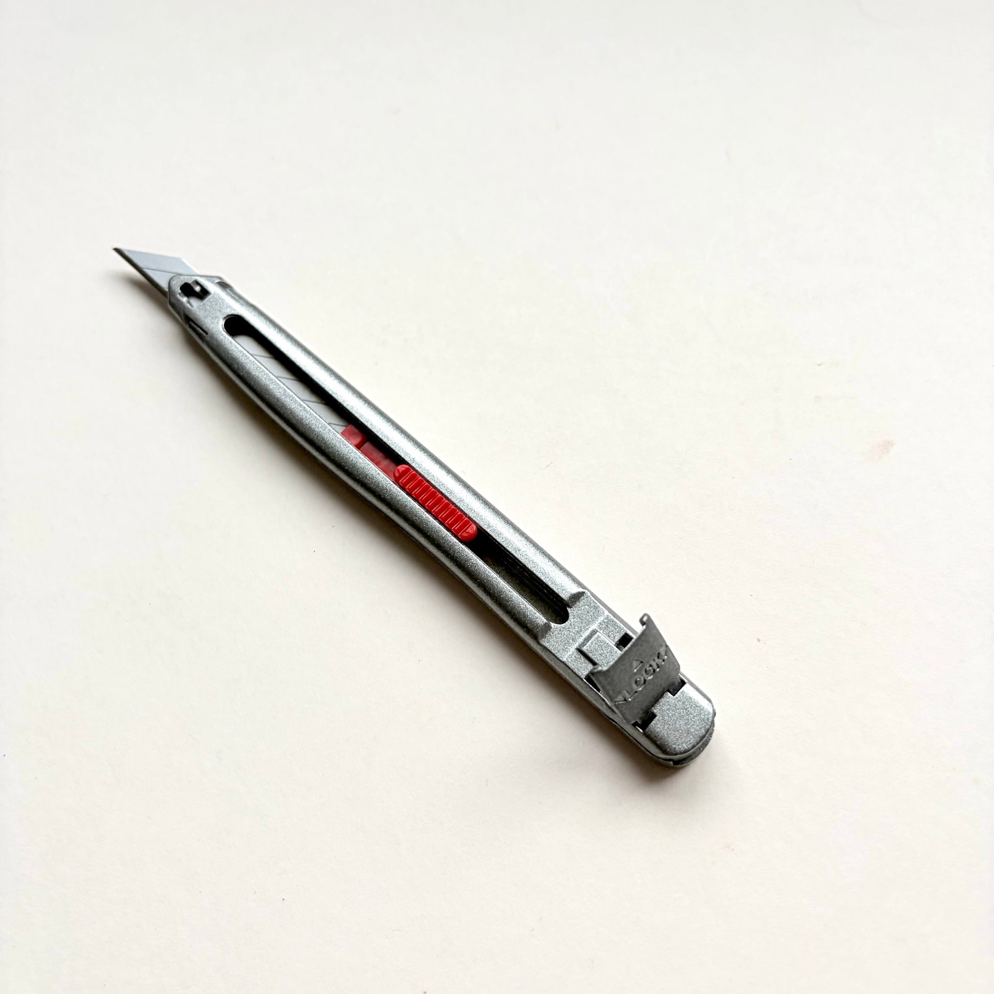 A silver Glanz utility knife with a red sliding scale indicator, shown diagonally on a plain off-white background.