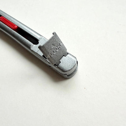 A silver Glanz utility knife with a red sliding scale indicator, shown diagonally on a plain off-white background.