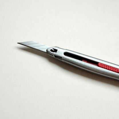 A silver Glanz utility knife with a red sliding scale indicator, shown diagonally on a plain off-white background.