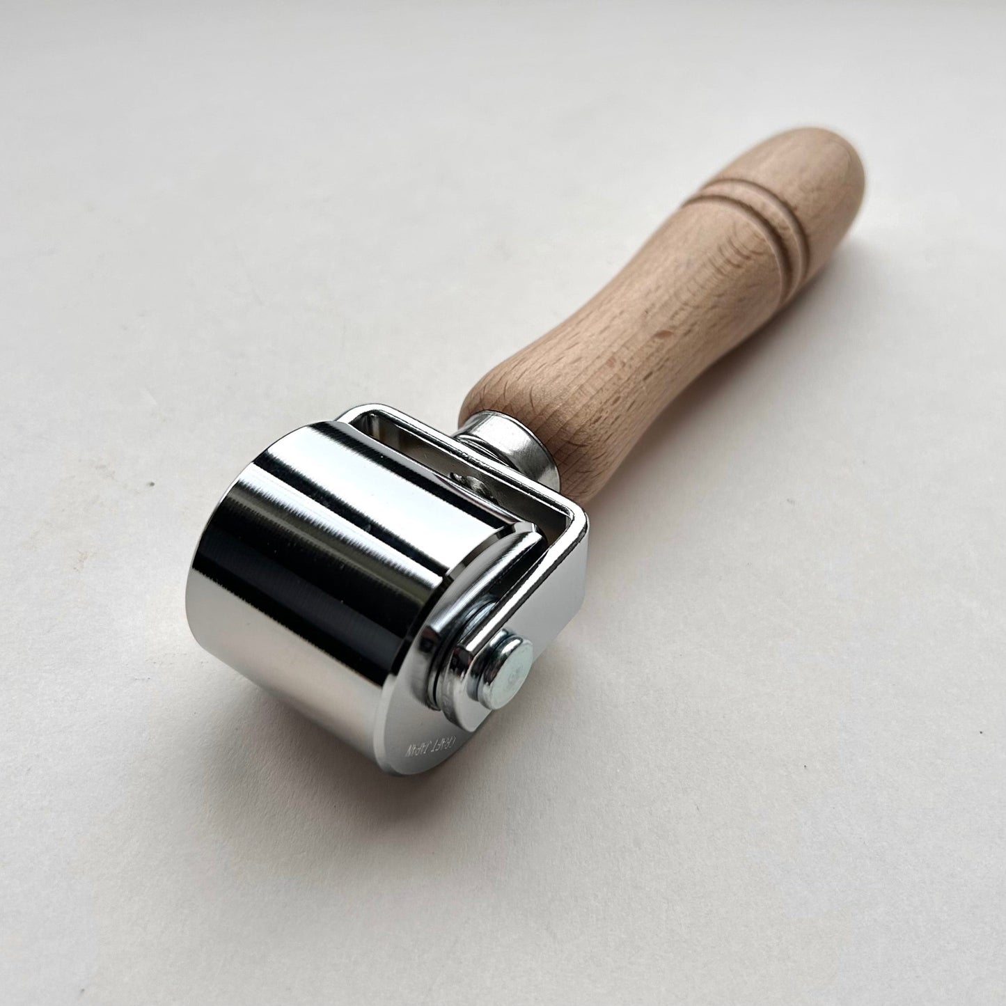 Metal roller with wooden handle on a light gray background