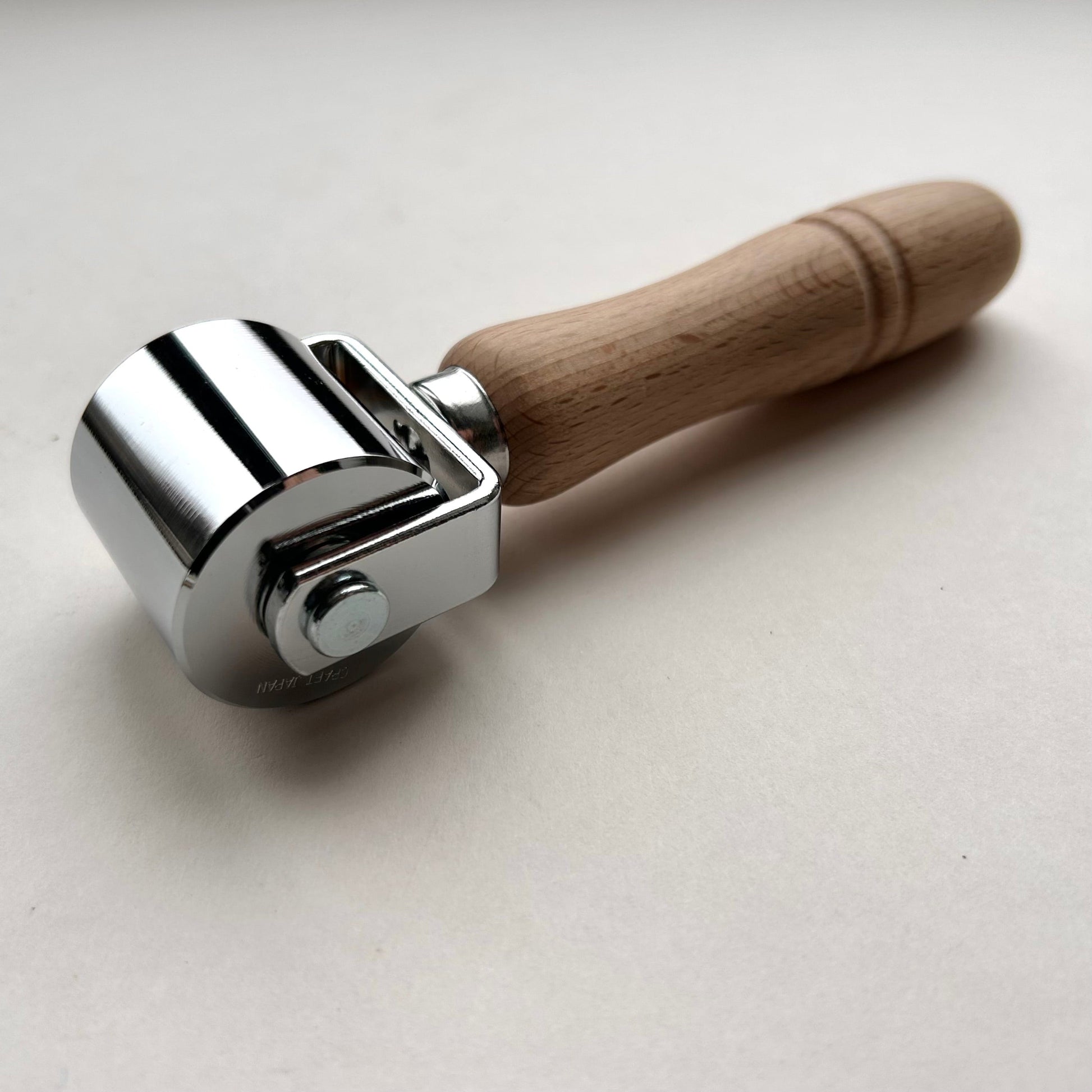 Metal roller with wooden handle on a light gray background
