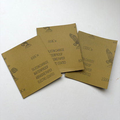 Three sheets of sandpaper fanned out on a white background, featuring brown abrasive paper with black printed text and eagle illustrations.
