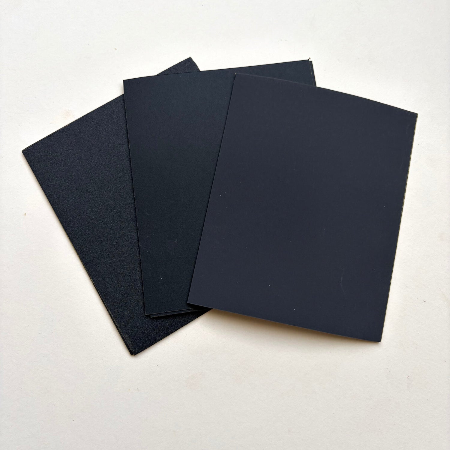 Black rectangular sheets of varying sized sand paper fanned out on a plain white surface.