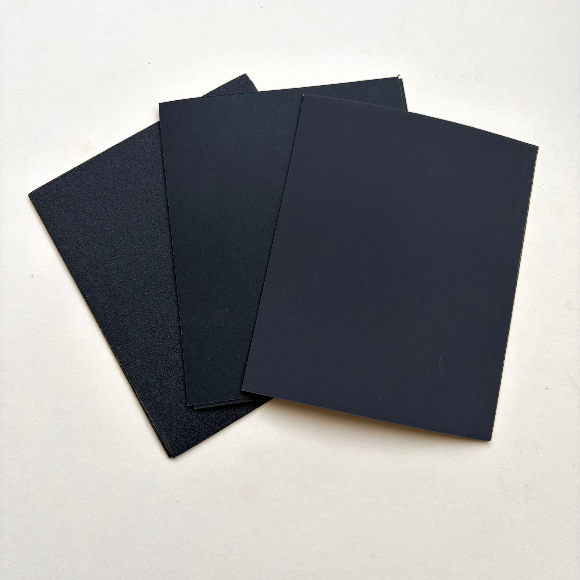Black rectangular sheets of varying sized sand paper fanned out on a plain white surface.