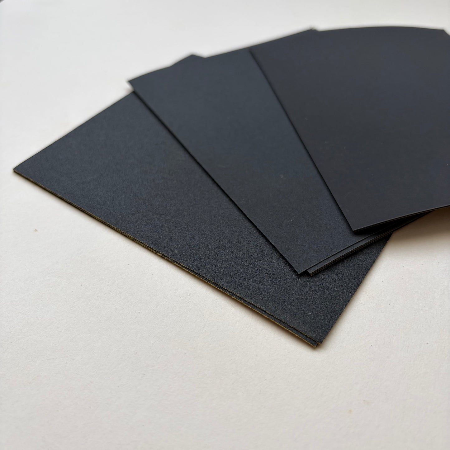 Black rectangular sheets of varying sized sand paper fanned out on a plain white surface.