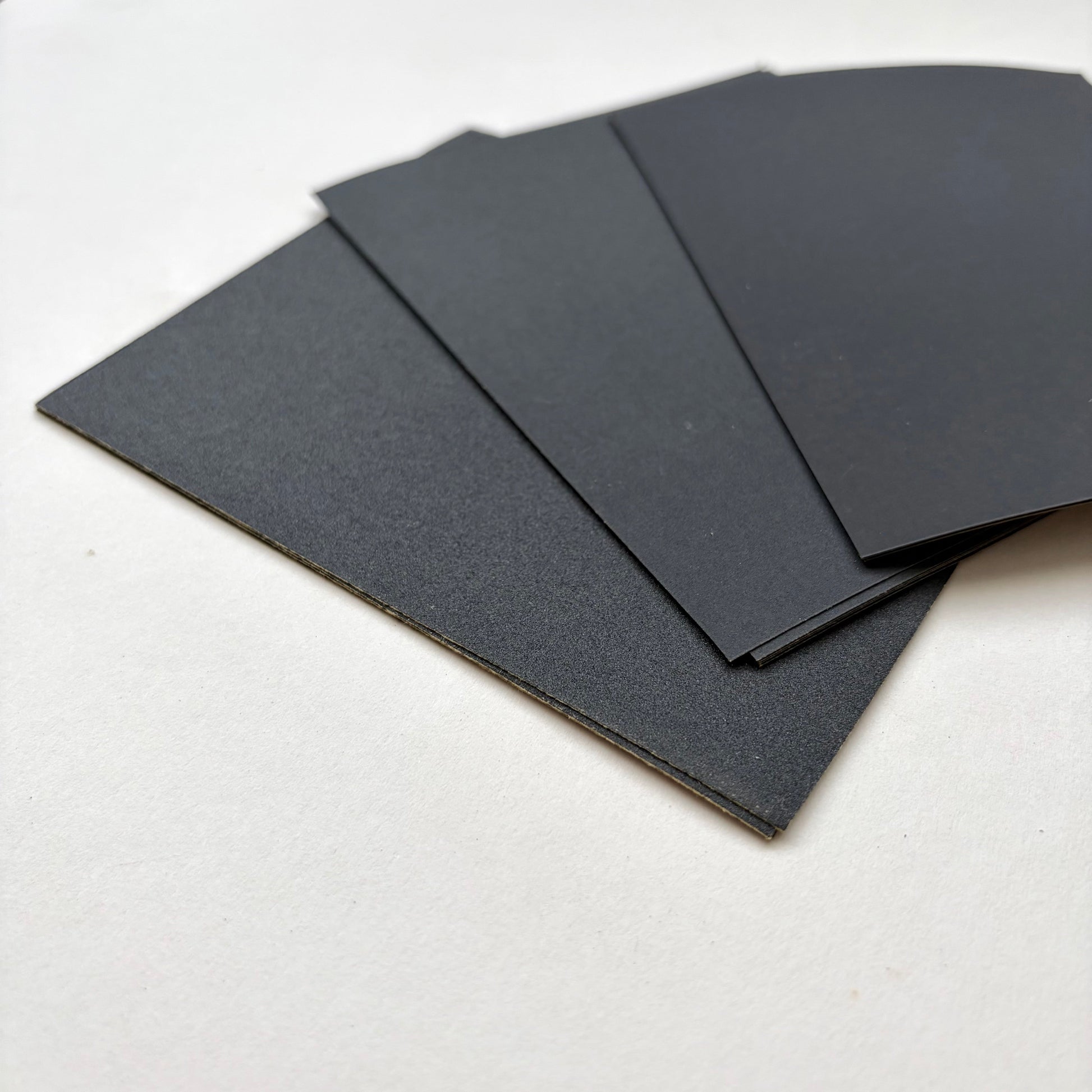Four black rectangular sheets of varying sized sand paper fanned out on a plain white surface.