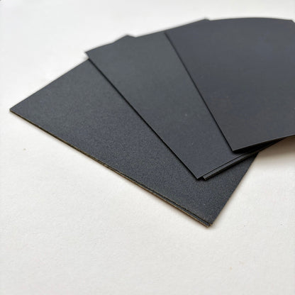 Four black rectangular sheets of varying sized sand paper fanned out on a plain white surface.