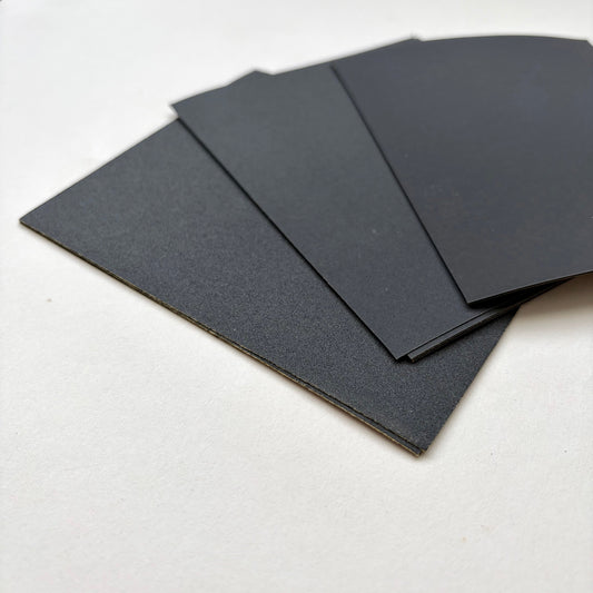 Four black rectangular sheets of varying sized sand paper fanned out on a plain white surface.