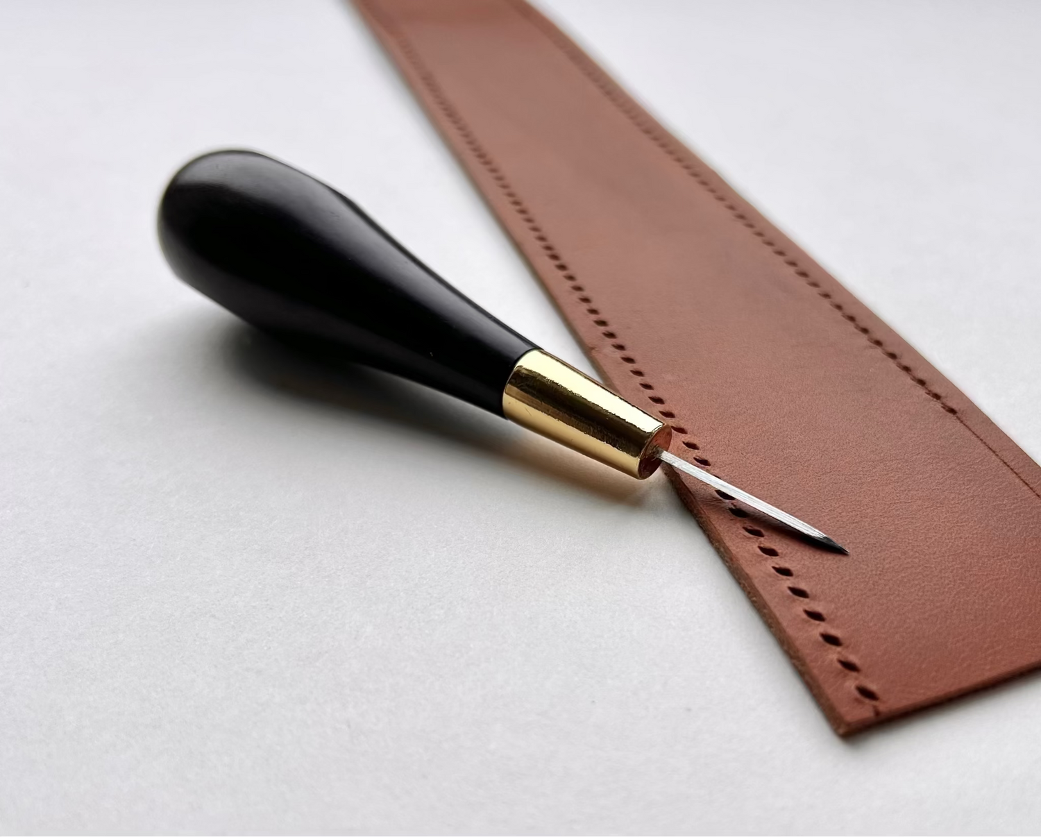 Brown leather strip with a leather tool on a light gray background
