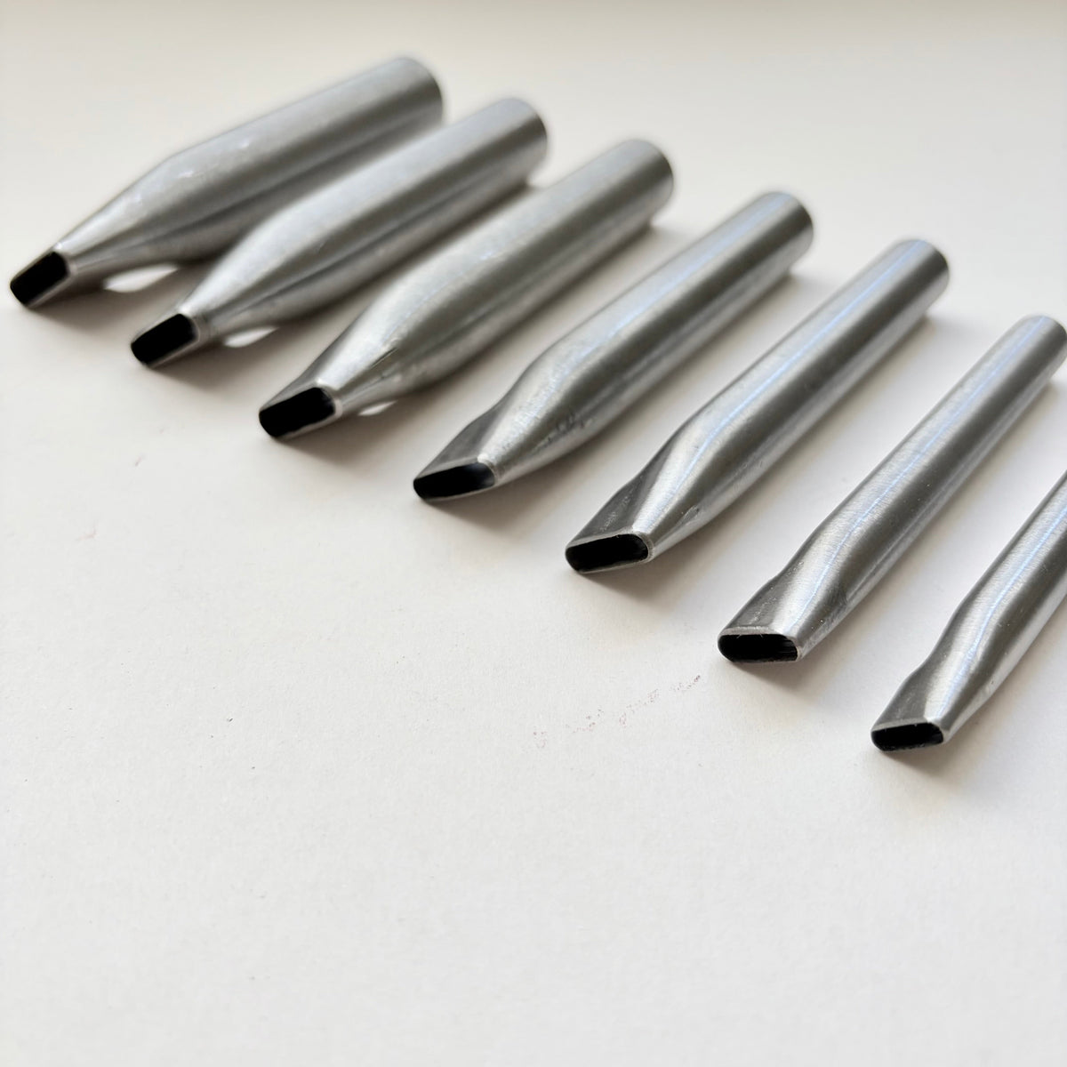 Six metallic oblong punches for leather on a white background