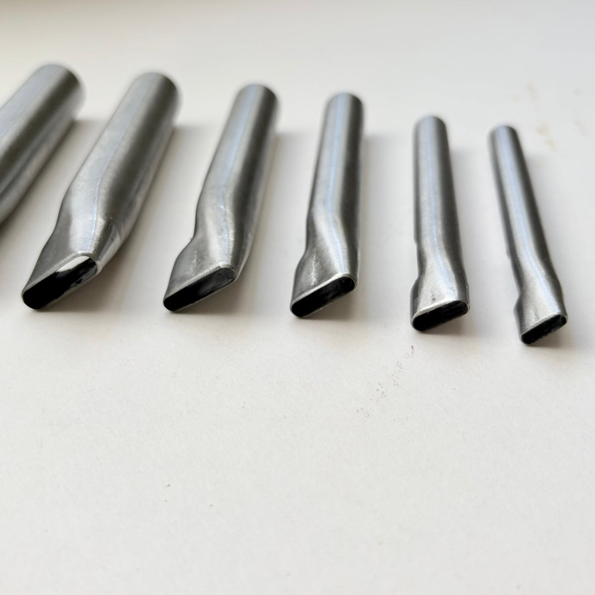 Six metallic oblong punches for leather on a white background