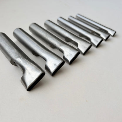 Six metallic silver metal punch tools arranged diagonally on a plain off-white surface.