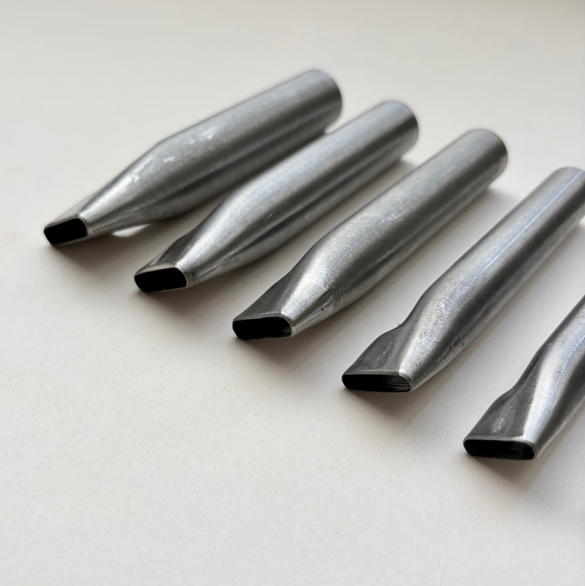 Six metallic oblong punches for leather on a white background