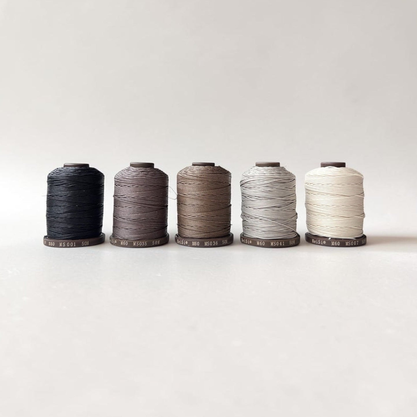 Five spools of Meisi linen thread in various colors on a white background