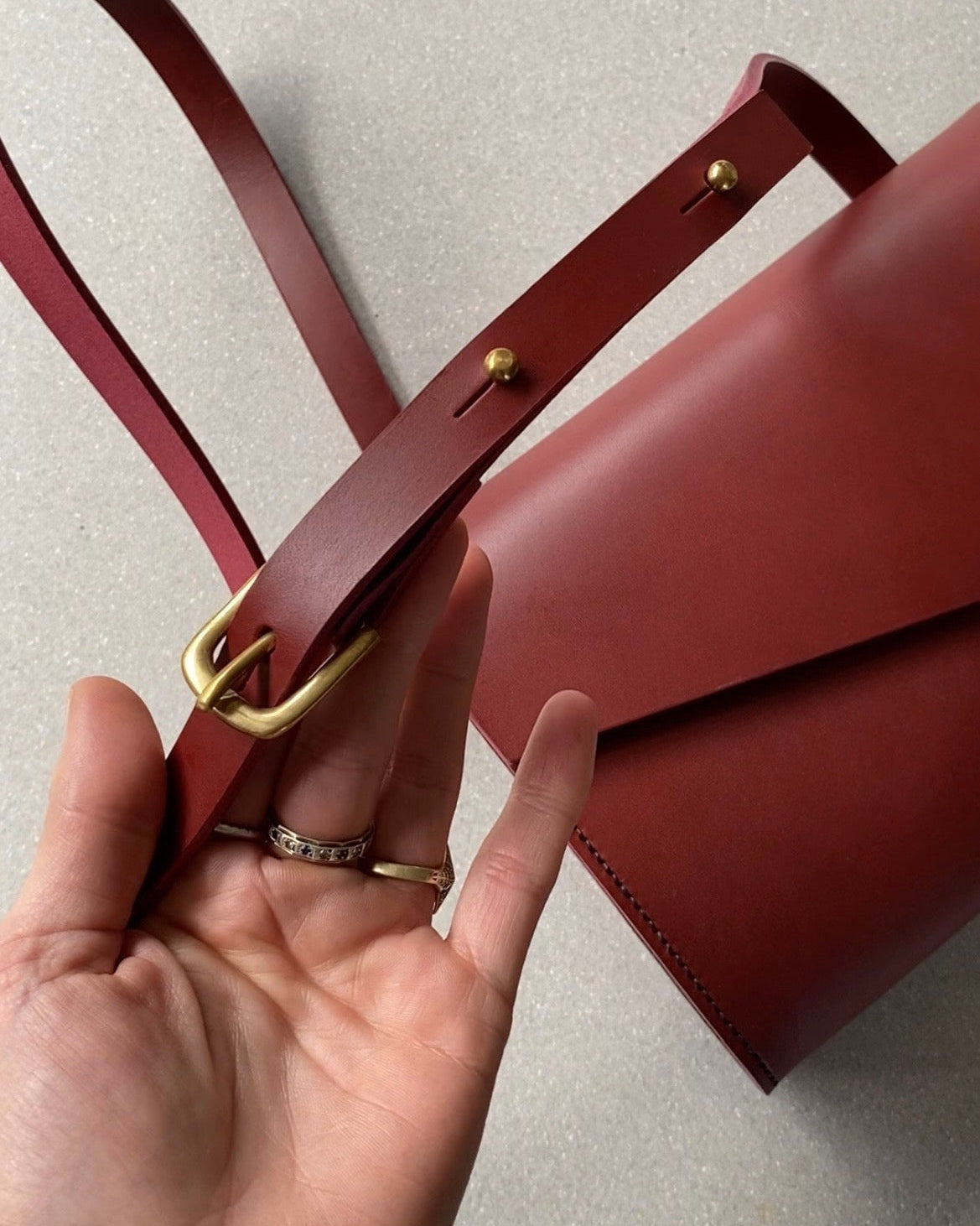Red handbag with gold solid brass West End buckle held by a hand on a light grey background