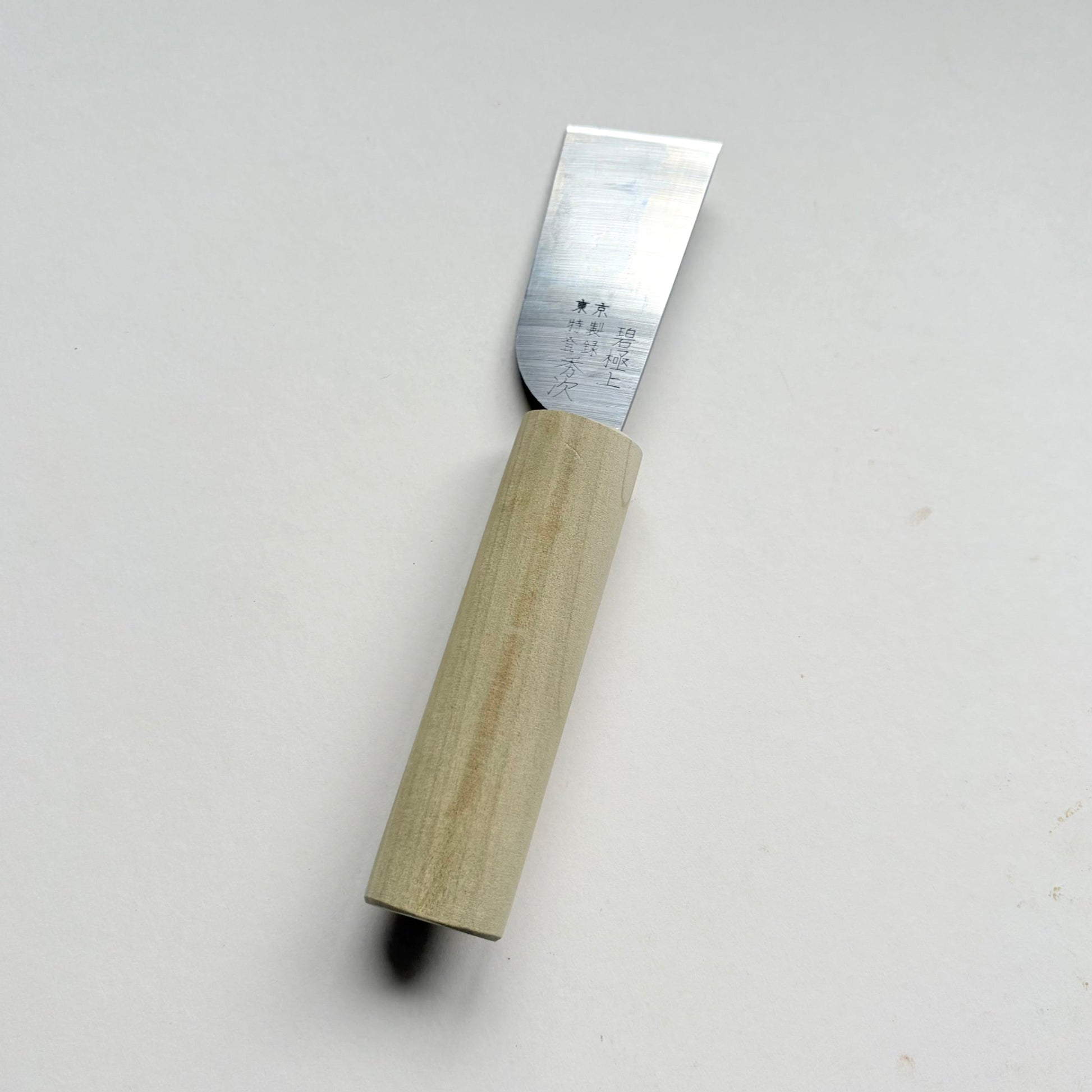 A Japanese-style wooden knife for leather with a light natural wood handle and a silver steel blade, photographed on a plain off-white background.