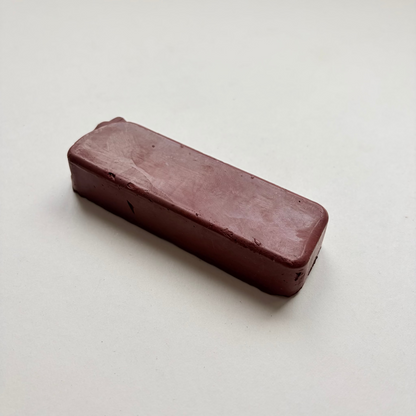 A rectangular, rounded-corner bar of dark reddish-brown jewellers rouge metal polishing compound on a plain off-white background.