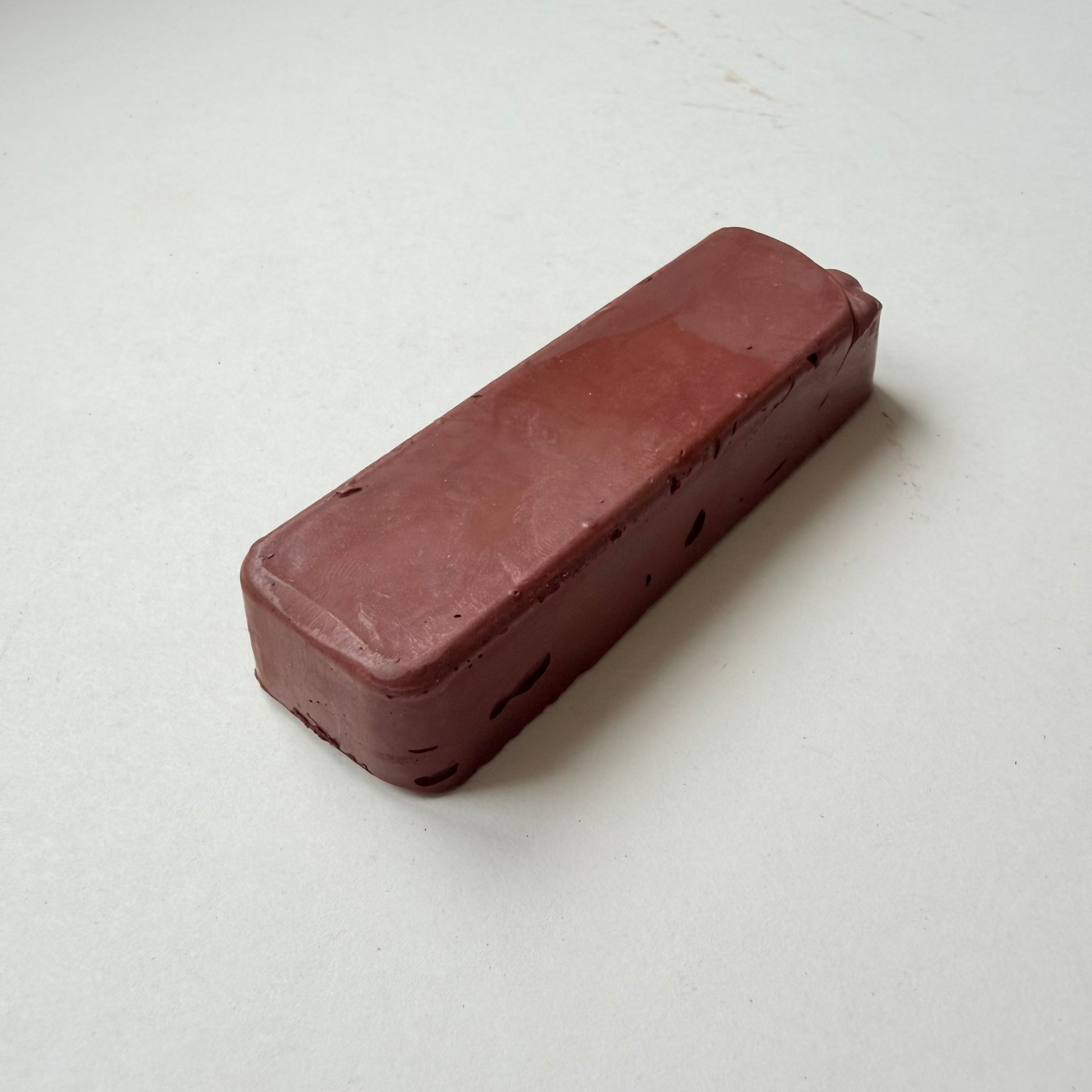A rectangular, rounded-corner bar of dark reddish-brown jewellers rouge metal polishing compound on a plain off-white background.