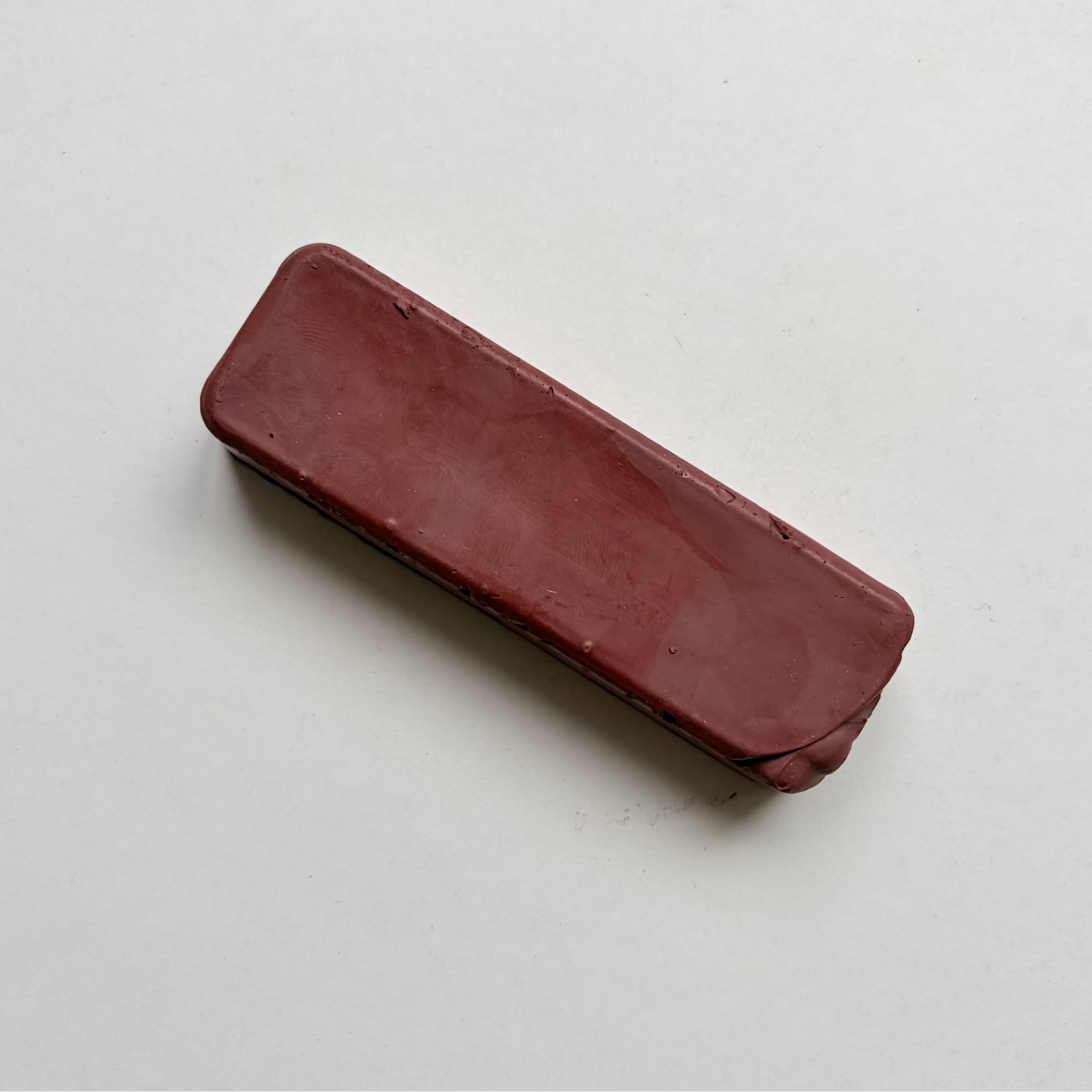 A rectangular, rounded-corner bar of dark reddish-brown jewellers rouge metal polishing compound on a plain off-white background.