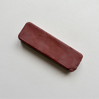 A rectangular, rounded-corner bar of dark reddish-brown jewellers rouge metal polishing compound on a plain off-white background.