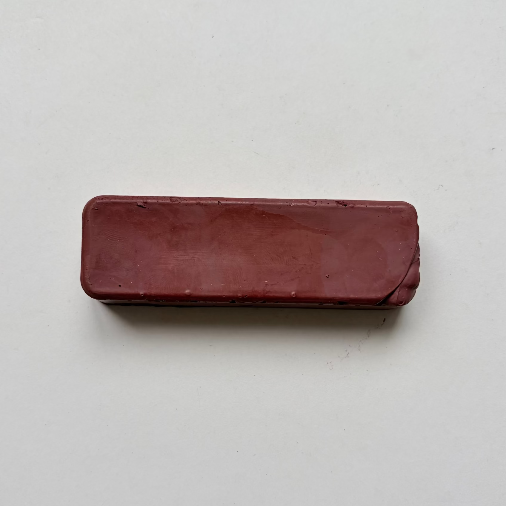 A rectangular, rounded-corner bar of dark reddish-brown jewellers rouge metal polishing compound on a plain off-white background.