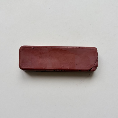 A rectangular, rounded-corner bar of dark reddish-brown jewellers rouge metal polishing compound on a plain off-white background.