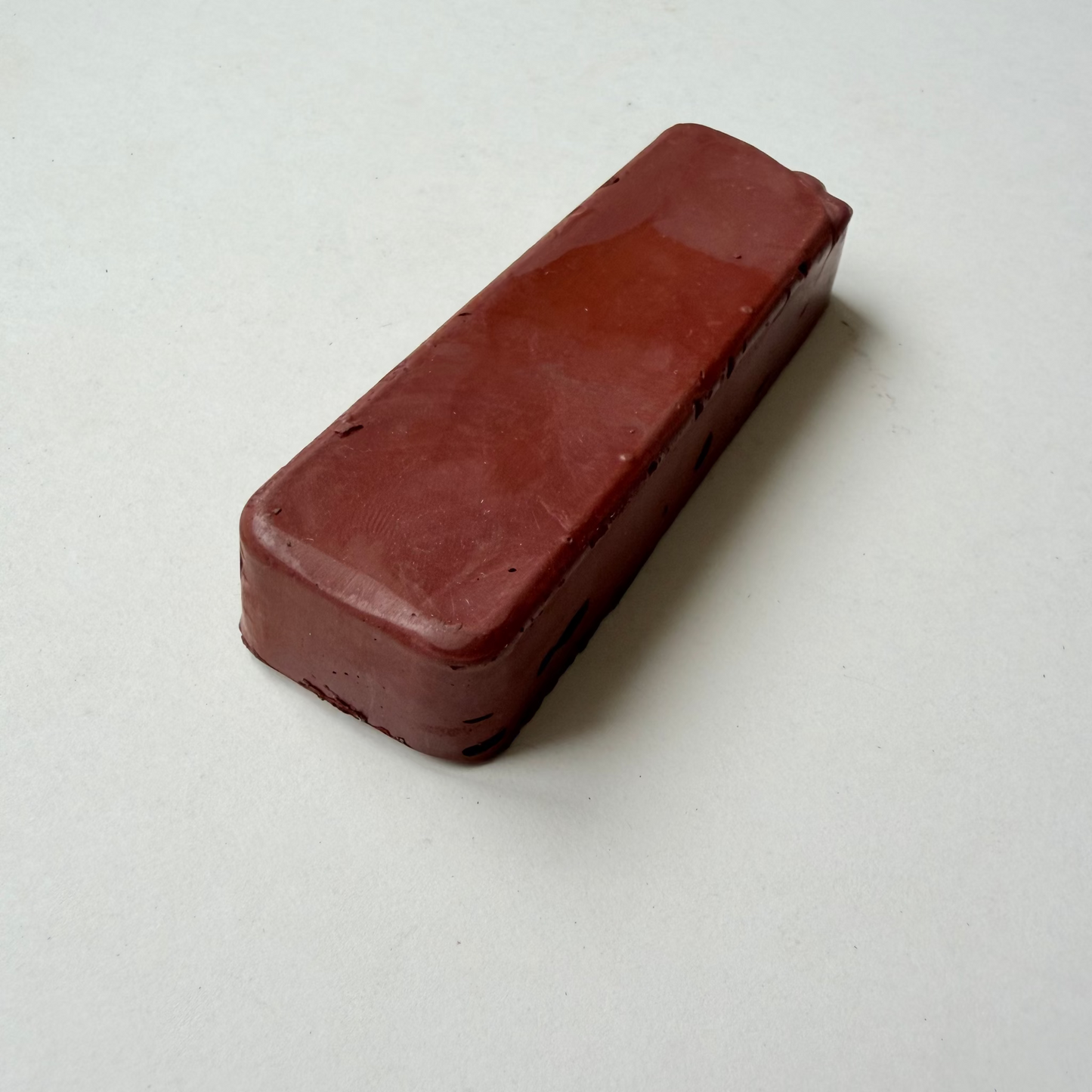 A rectangular, rounded-corner bar of dark reddish-brown jewellers rouge metal polishing compound on a plain off-white background.