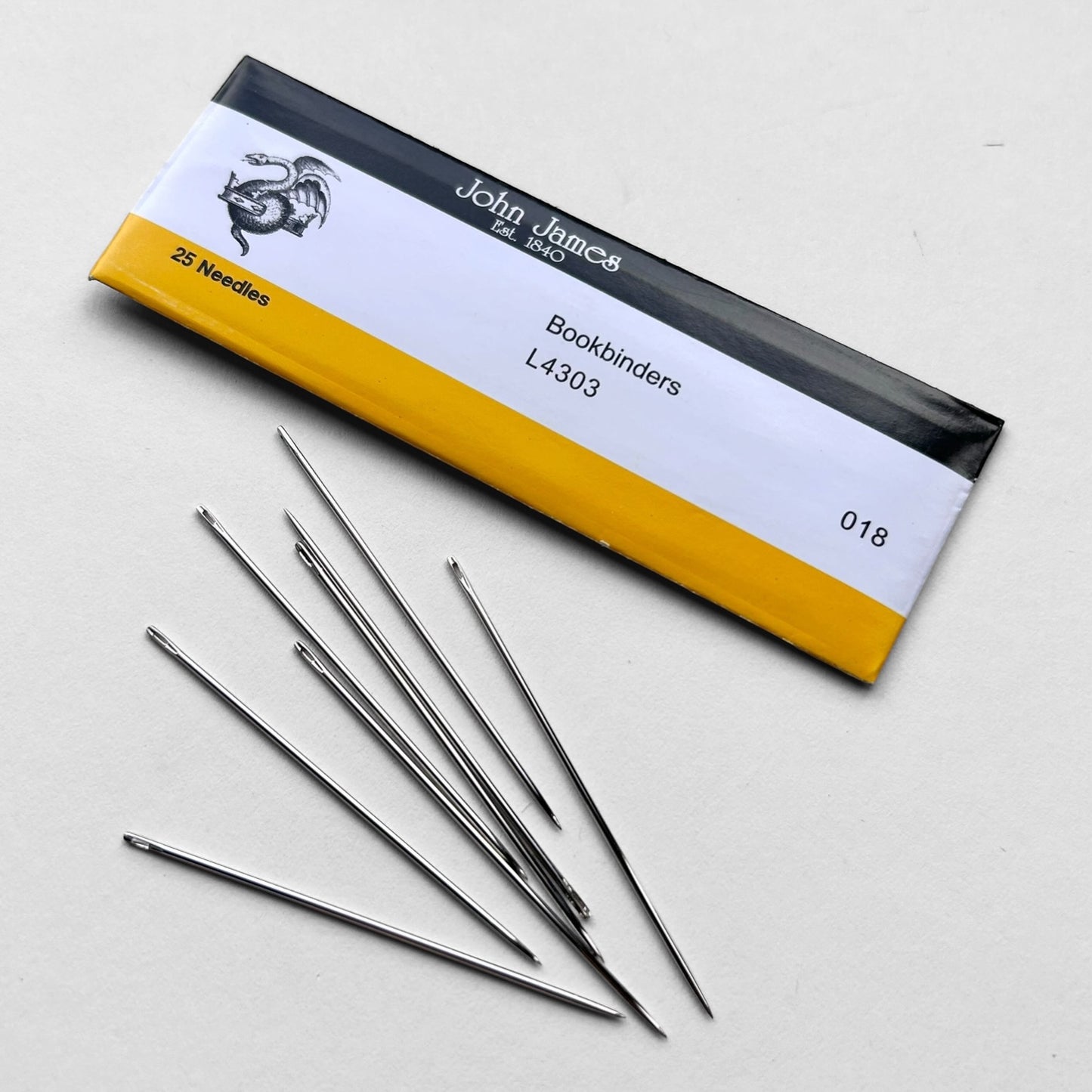Box of John James bookbinding needles with needles spilling out on a light gray background