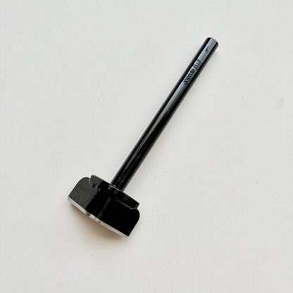 A black metal corner punch for leather with a long straight black handle, photographed on a plain light grey background.
